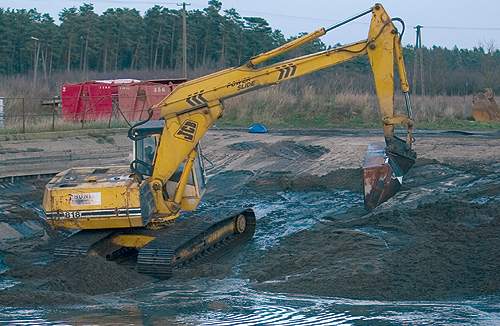 En gravko læsser tonsvis af lort fra bunden af en af Poldanors gyllelaguner op på en traktor med vogn, som spreder det på de tisltødende marker. (Michael Daugaard)