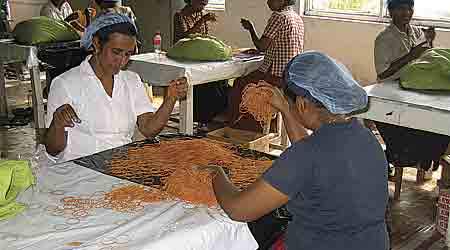 Hen ved tyve kvinder sidder og stopper dagens produktion på 1.000 kilo brune gummibånd i kasser. Som de eneste på Ceytra Limited bærer de beskyttelse. Et blåt hårnet, så der ikke kommer hår ned i papkasserne til elastikkerne. (Foto: Morten Halskov)