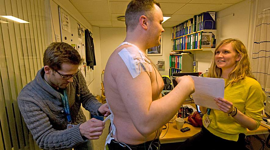 Bagageportør Christoffer Nyland får monteret elektroder på kroppen af Phd-studerende Henrik Koblaub og Stine Hvid Bern. På den måde måler de, hvordan arbejdet påvirker musklerne. (Foto: Harry Nielsen)
