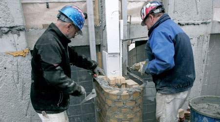 Billedtekster: Murersvendene Andre Stender (tv) og Leif Broe i gang med at skalmure en søjle. En skabelon, der glider på en skinne, holder stenene på plads.
 (Foto: Harry Nielsen)